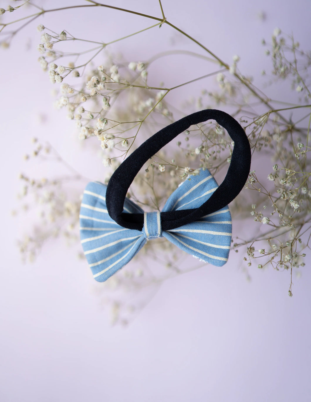 A rear view of the blue and white printed lace bow hair accessory with a band, on a serene background. 