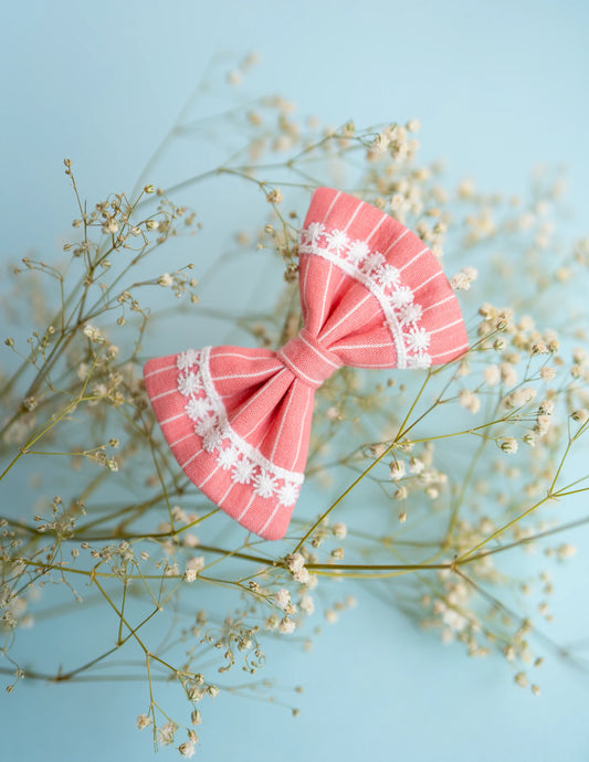 An image of a pink lace bow hair accessory, with pretty white print throughout, on a serene light blue background.
