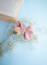 Load image into Gallery viewer, A zoomed out view of Daisy delight knot Hairclip for girls. Hair Accessories with a flowery design, with an open book on a light blue background.
