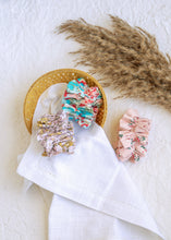 गैलरी व्यूवर में इमेज लोड करें, hair accessories of three Floral Scrunchies placed in a wooden basket with a white cloth beneath, placed on a white background with some leaves for decoration
