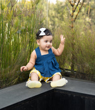 Load image into Gallery viewer, A picture of a baby girl wearing a Cotton Bow Hair Clip for hair accessories sitting on a bench with plants in background