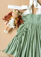Load image into Gallery viewer, An elegant and beautiful secret fairy pocket dress for baby girl dresses kept on a peach background with some flowers and toy aside.
