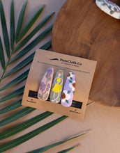 Load image into Gallery viewer, Photo of a set of three Linen Tic Tac Embroidery Hair Clips in pastel colors. Each clip features a rectangular linen base with delicate embroidery details in different patterns and colors with green leaves beneath it, on a wooden tray