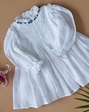 गैलरी व्यूवर में इमेज लोड करें, The pintuck detailing across the bust and ruffles running across the neckline in classic white palette kept upon a peach background with some leaf and flower aside.