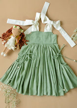 गैलरी व्यूवर में इमेज लोड करें, An elegant and beautiful secret fairy pocket dress for baby girl dresses kept on a peach background with some flowers and toy aside.