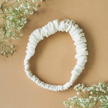 Load image into Gallery viewer, A beautiful ruffled white headband kept upon a light peach background with some flowers aside.
