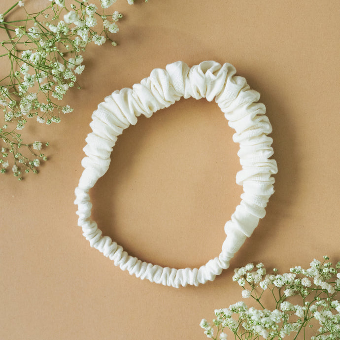 A beautiful ruffled white headband kept upon a light peach background with some flowers aside.