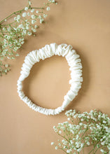 Load image into Gallery viewer, A beautiful ruffled white headband kept upon a light peach background with some flowers aside.