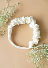 Load image into Gallery viewer, A beautiful ruffled white headband kept upon a light peach background with some flowers aside.
