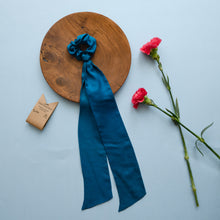 गैलरी व्यूवर में इमेज लोड करें, A beautiful blue silk hair scrunchie kept upon a round wooden log with some flowers and brown card aside.