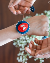 गैलरी व्यूवर में इमेज लोड करें, A man tying a handmade spiderman rakhi to child with some flower in the background.