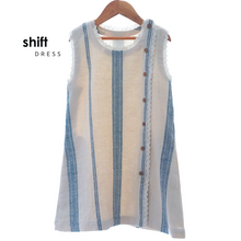 Load image into Gallery viewer, A beautiful white A-line shift dress with flattering vertical blue stripes and laced hemline is hanged using hanger.
