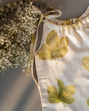 Load image into Gallery viewer, A cute baby girl dress made of eco-printed Indian maple leaves on it along with some flower aside.
