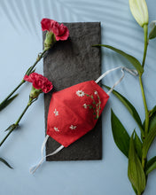 Load image into Gallery viewer, A red color organic cotton hand-embroidered adjustable face masks kept upon a grey sheet with some flowers aside.