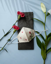Load image into Gallery viewer, A white color organic cotton hand-embroidered adjustable face masks kept upon a grey sheet with some flowers aside.