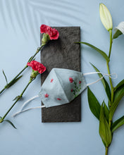 Load image into Gallery viewer, A light grey color organic cotton hand-embroidered adjustable face masks kept upon a grey sheet with some flowers aside.