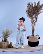 गैलरी व्यूवर में इमेज लोड करें, A baby girl wearing cute jumpsuit with matching hair accessories with some artificial plants and wooden pots and with some rabbit toys and a flower basket aside.