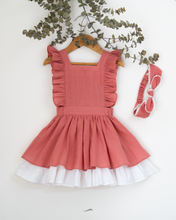 Load image into Gallery viewer, A beautiful dress with a criss-cross back hung on a hanger with a matching hair accessory beside it with a stem of leaves upon it.
