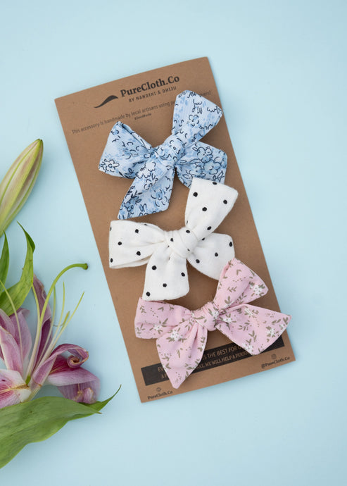An image of three elegant knot combo hairclips for girls, one in white colour with small black dots, the other in a pinkish flowery print, and a third with light blue floral print, on a light blue background.