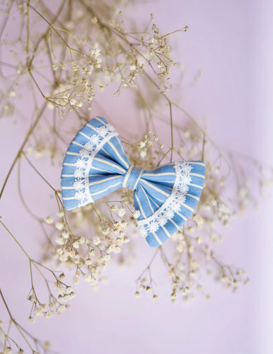 An image of a blue lace bow hair accessory, with pretty white print throughout, on a serene background.