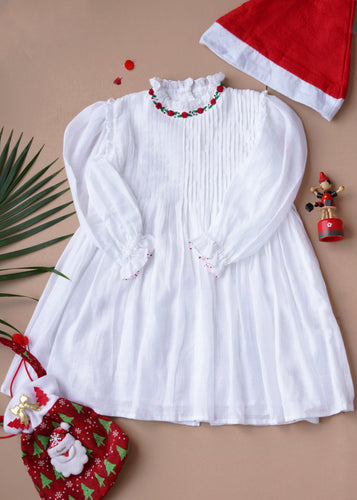 Beautiful white dress with pintuck detailing across the bust and ruffles running across the neckline with a Christmas hat, a toy, a Christmas bag and a leaf.