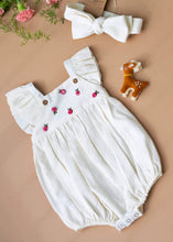 Load image into Gallery viewer, A white baby girl dress with head band and a cute little deer-friend is kept on a light peach background with some flowers aside.
