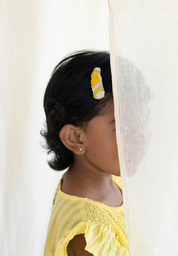 A picture of kid behind a curtain, half visible who is wearing an Embroidery Tic Tac Hair Clip for hair accessories