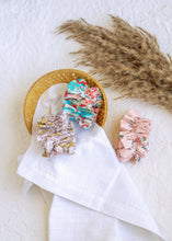 Load image into Gallery viewer, hair accessories of three Floral Scrunchies placed in a wooden basket with a white cloth beneath, placed on a white background with some leaves for decoration
