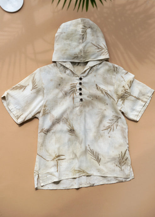 A unisex hooded kurta eco-printed using silver oak leaves kept upon a peach background.