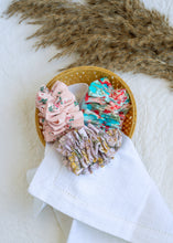 Load image into Gallery viewer, hair accessories of three Floral Scrunchies placed in a wooden basket with a white cloth beneath, placed on a white background with some leaves for decoration
