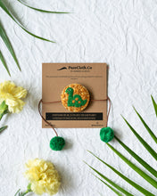 गैलरी व्यूवर में इमेज लोड करें, Handmade Dinosaur Rakhi wrapped around brown card with flower and leaf aside.
