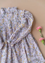 Load image into Gallery viewer, A beautiful lavender fairy floral baby girl dress with frills at the neck kept upon a peach background with some flowers aside

