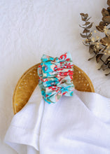 Load image into Gallery viewer, A hair accessory of Blue Floral Scrunchies placed in a wooden basket with a white cloth beneath, placed on a white background with some leaves and decoratives
