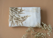 Load image into Gallery viewer, A beautiful muslin baby swaddle with silver oak leaves eco printed on it with a flower aside.
