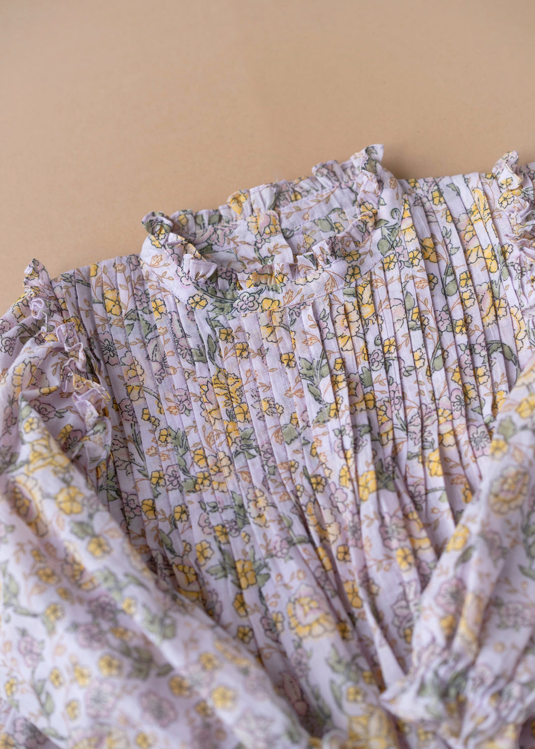 A close view of a beautiful lavender fairy floral baby girl dress with frills at the neck kept upon a peach background