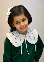 गैलरी व्यूवर में इमेज लोड करें, A young kid wearing the white combo of detachable victorian style collar and matching bow with subtle hand embroidery upon dark green top standing in front of a white background.
