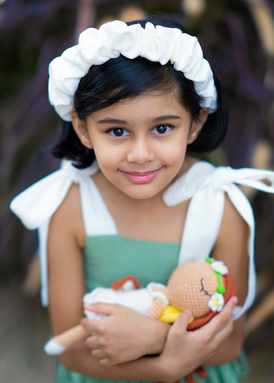 A girl wearing ruffled white headband and also holding a toy.