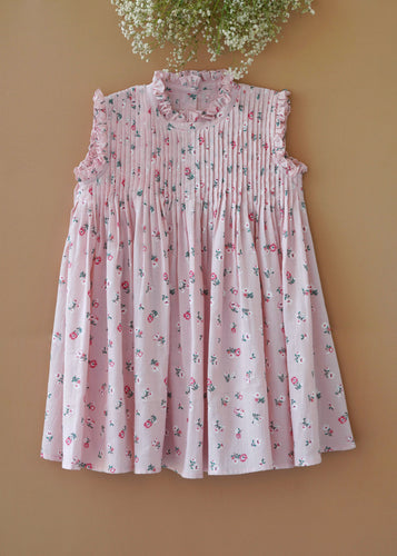 A beautiful pink fairy floral dress with frills at the neck kept upon a peach background with some flowers aside.