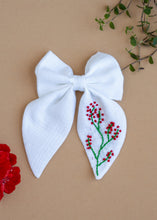 गैलरी व्यूवर में इमेज लोड करें, A Red Embroidered White Hairclip for kids hair accessories placed on a light brown background with flowers and leaves as decor

