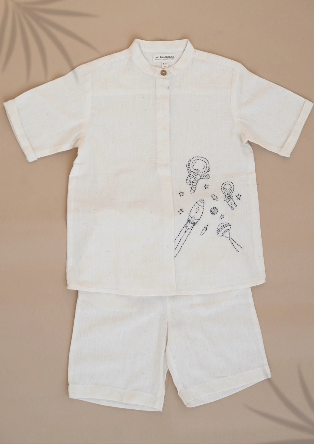 A set of white coloured Organic Cotton Doodle Shirt and Cargo Shorts kidswear kept on a biege coloured background