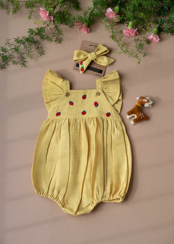 A yellow baby girl dress with head band and cute little deer-friend is kept on a baby pink background with some  flowers aside. 
