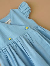 Load image into Gallery viewer, A designer light indigo flutter sleeve wrap dress kept upon a light peach background.
