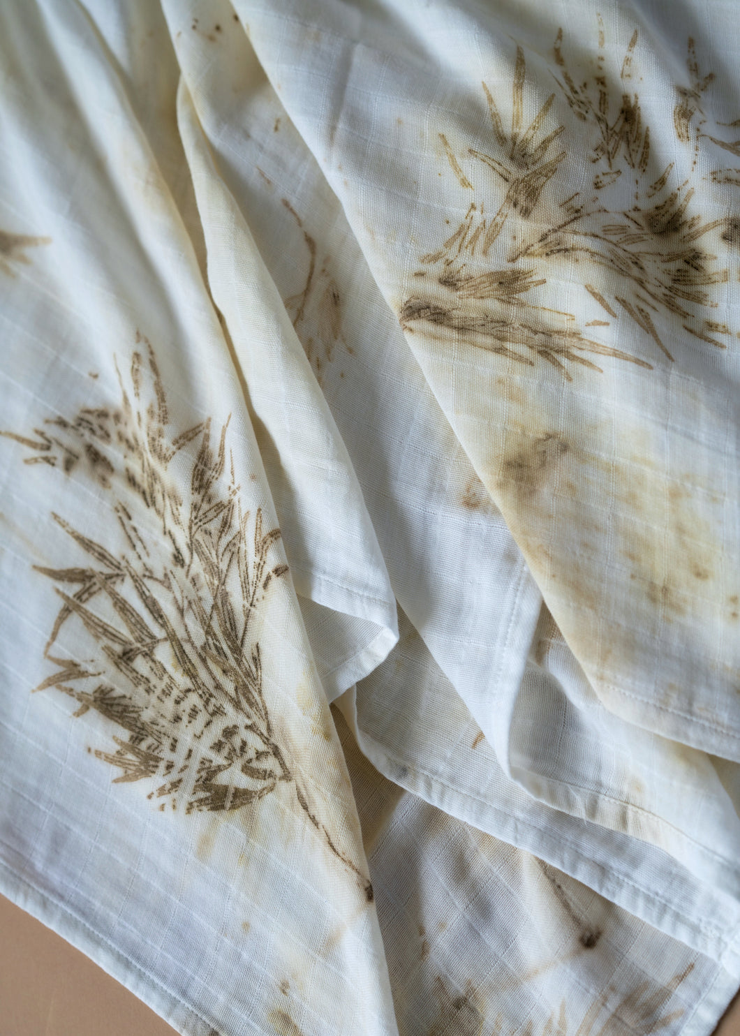 A beautiful muslin baby swaddle with silver oak leaves eco printed on it.