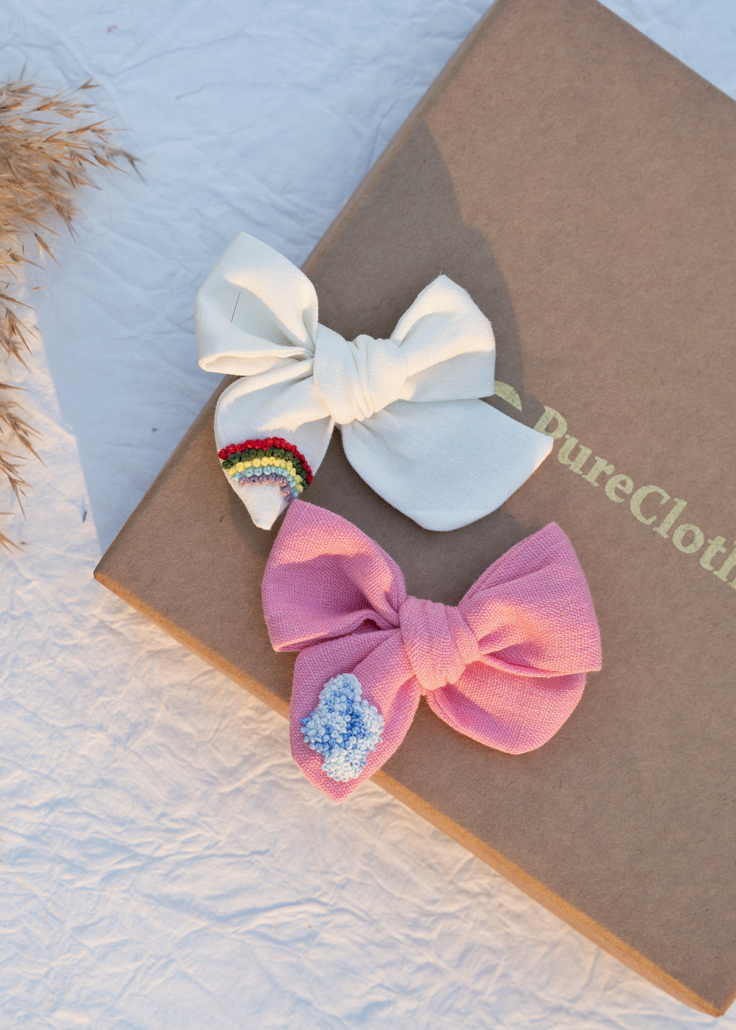 Two (Off-white and Pink) Hair Clips tied to one another on top of a box.