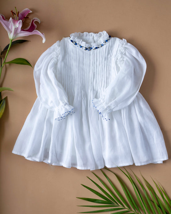 The pintuck detailing across the bust and ruffles running across the neckline in classic white palette kept upon a peach background with some leaf and flower aside.