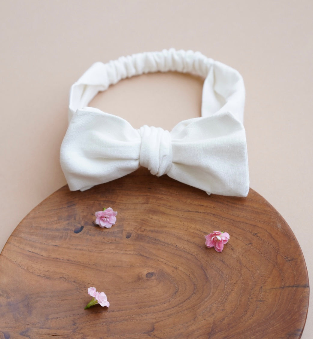 A bow type white hair accessories placed on a brown plate with a cute small flowers  aside.
