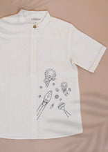 गैलरी व्यूवर में इमेज लोड करें, A white coloured Organic Cotton Doodle Shirt kidswear with space theme design kept on a biege coloured background
