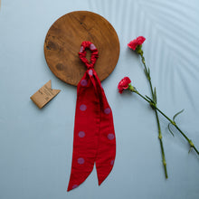 Load image into Gallery viewer, A beautiful red silk hair scrunchie kept upon a round wooden log with some flowers and brown card aside.
