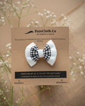 Load image into Gallery viewer, A mini black and white hair accessory tied on a brown card with some flowers in the background.
