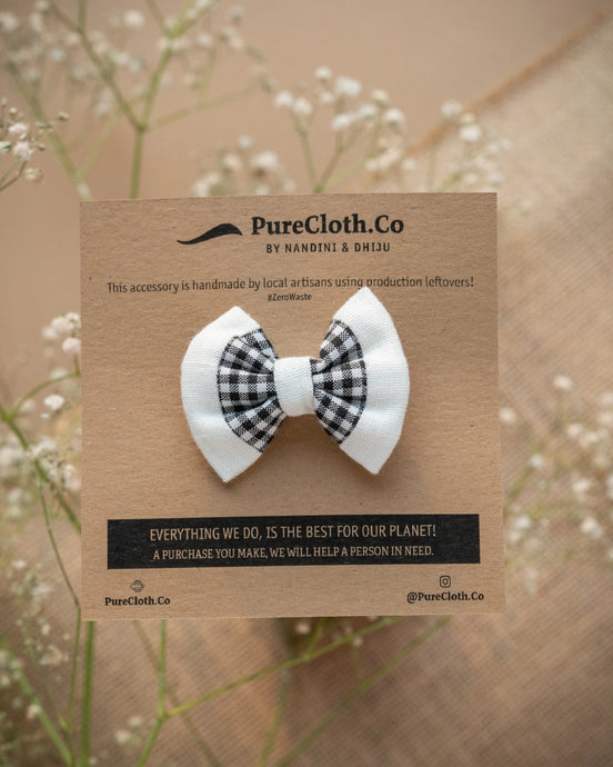 A mini black and white hair accessory tied on a brown card with some flowers in the background.